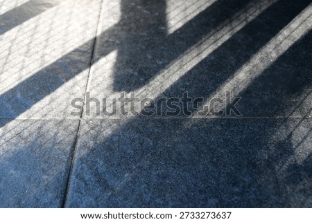 Floor features bold diagonal shadows from a railing, creating a moody geometric composition. The interplay of light and texture evokes urban architecture and a calm, cool ambiance.