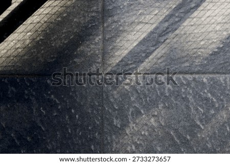 Floor features bold diagonal shadows from a railing, creating a moody geometric composition. The interplay of light and texture evokes urban architecture and a calm, cool ambiance.