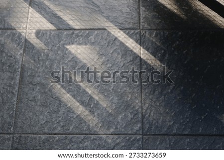 Floor features bold diagonal shadows from a railing, creating a moody geometric composition. The interplay of light and texture evokes urban architecture and a calm, cool ambiance.