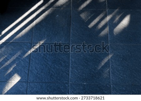 Floor features bold diagonal shadows from a railing, creating a moody geometric composition. The interplay of light and texture evokes urban architecture and a calm, cool ambiance.