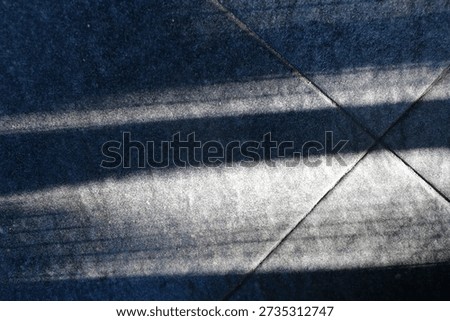 Floor features bold diagonal shadows from a railing, creating a moody geometric composition. The interplay of light and texture evokes urban architecture and a calm, cool ambiance.