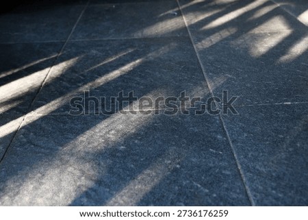Floor features bold diagonal shadows from a railing, creating a moody geometric composition. The interplay of light and texture evokes urban architecture and a calm, cool ambiance.