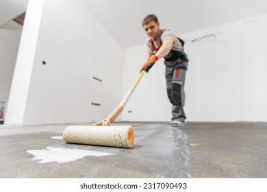 Floor priming process. Worker use primer on concrete floor before laying tiles, strengthening surface.