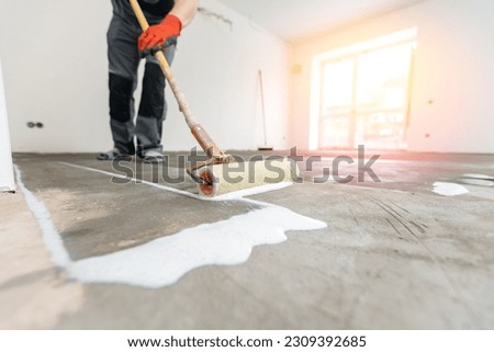 Floor priming process. Worker use primer on concrete floor before laying tiles, strengthening surface.