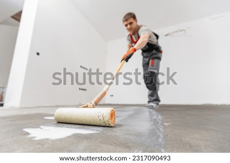 Floor priming process. Worker use primer on concrete floor before laying tiles, strengthening surface.