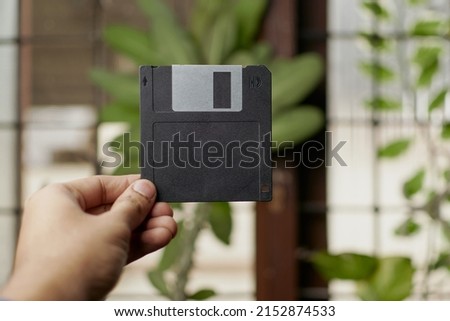 Floppy disk in hand with window and green indoor plant backdround