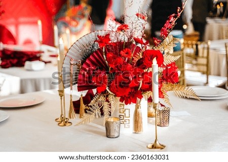 Floral arrangement, festive bouquet, table decoration for Chinese New Year party celebration in restaurant. Traditional red gold color decor. Roses,poppies,fan,candles,tassels. Chinese lunar calendar.