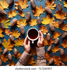 Blumentherbsthintergrund. Ein Schlamm Kaffee in der Hand einer Frau in einem Pullover auf grünem Hintergrund mit gelben fallenden Blättern Ahorn und Zapfen. Hallo Herbst. Flaches Laien Instagram Mode Getränk Komposition.