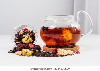 Floral black tea brewed in a transparent teapot. A hot drink on the table with a scattering of tea collection from dried flowers. Opening of tea flowers in hot water. Beautiful tea. ceremony tradition