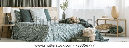 Floral design of bright bedroom interior with green blankets, straw hat and traveler's suitcase