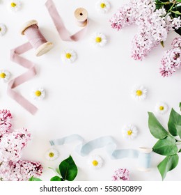 Floral Frame Of Lilac Flowers, Chamomile, Fresh Branches And Spool With Blue And Beige Ribbon On White Background. Flat Lay, Top View