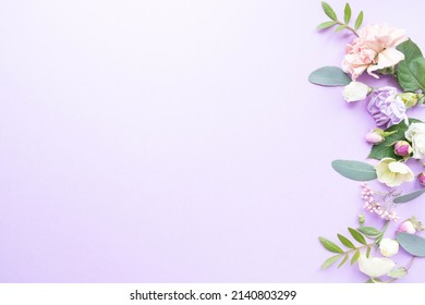 Floral frame with pink roses, white flowers, branches, leaves and petals on purple background. Flat lay, top view