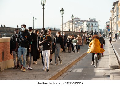 Florence, Italy - 2021, February 21: People on the bike path, cycling along the Arno river and walking on the sidewalk, wearing protective masks.
