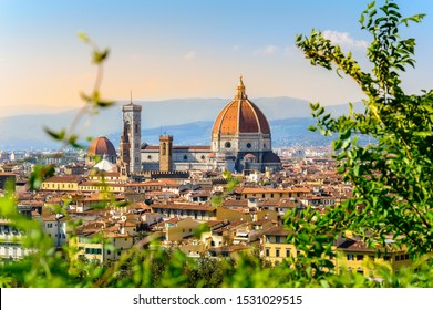 Florence, Italy: scenic view on Florence old town with Duomo Cathedral of Santa Maria del Fiore and Giotto's Bell Tower from Michelangelo square at sunset with defocused green leaves in front
