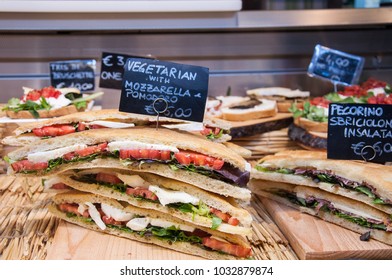 Florence, Tuscany /Italy - February 23, 2018. Sandwich Of Bread Stuffed With Mozzarella, Green Cucumber And Black Olives, Lettuce Leaves, On The Plates Are The Names Of Sandwiches And The Price 