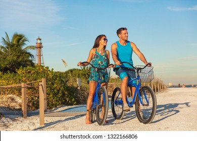 Florida Beach Vacation Couple Biking Sport Rental Bikes Recreational Activity Happy Watching Sunset On Sanibel Island By The Lighthouse. Young Woman And Man Riding Bicycles. Summer People Lifestyle .