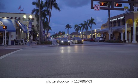 Florida, USA - Circa 2018: Downtown Delray Beach Street And Shopping Strip Mall During Dusk Evening Just After Sunset On A Beautiful Summer Night. Nightlife Traffic Wait At Intersection Stop Light