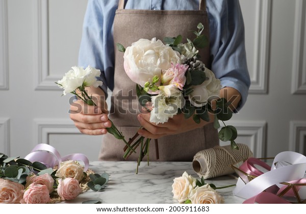 Florist creating beautiful bouquet at white\
marble table, closeup