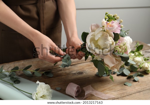 Florist creating beautiful bouquet at wooden\
table indoors, closeup