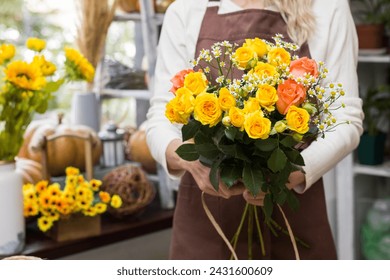 Florist holding a bouquet in a flower shop.Bouquet in the hands of a flower shop seller.Flower seller in an apron.floristry and flower arrangement training courses.Bouquet in hands close-up - Powered by Shutterstock