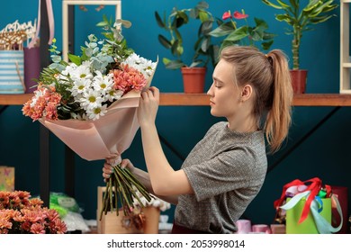 Florist macht einen Strauß. Ein junges erwachsenes Mädchen hält einen großen Strauß mehrfarbiger Chrysanthemen in den Händen und überprüft ihn.
