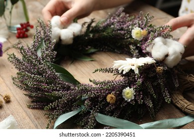Florist making beautiful autumnal wreath with heather flowers at wooden table, closeup