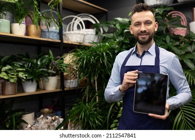florist man demonstrates the screen of the tablet against the background of potted plants