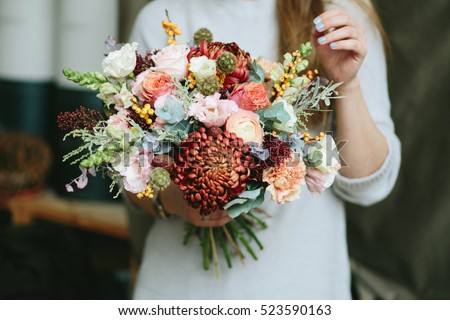 Florist shop in daylight. Woman holding beautiful bouquet of flowers. Florist with her work. Stylized tender photo with hipster filter. 