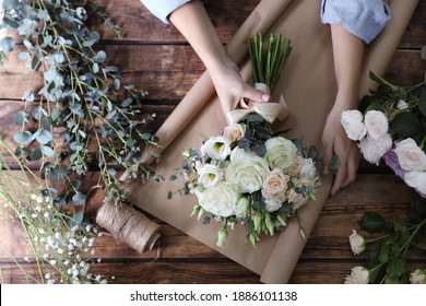 Florist wrapping beautiful wedding bouquet with paper at wooden table, top view