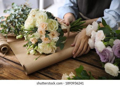 Florist wrapping beautiful wedding bouquet with paper at wooden table, closeup - Powered by Shutterstock