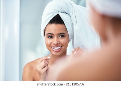 Floss for a cleaner smile. Shot of a woman flossing her teeth while wearing a towel wrapped around her head.
