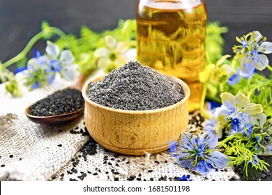 Flour Of Black Caraway In A Bowl, Seeds In A Spoon On Burlap, Oil In Bottle And Twigs Nigella Sativa With Blue Flowers And Leaves On Wooden Board Background