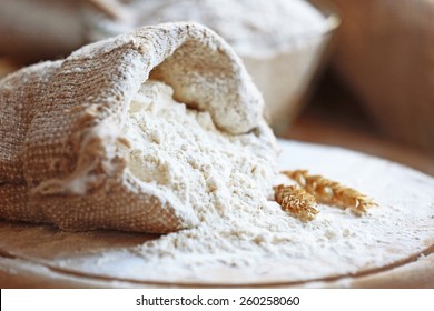 Flour in burlap bag on cutting board and wooden table background