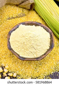 Flour corn in a clay bowl on the grits, cobs and grains, a bag on a wooden boards background