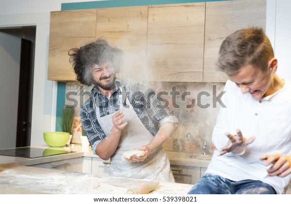 Flour fight in kitchen. Father and his son\
preparing a cake in the\
kitchen