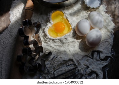 Flour On A Table With A Cookie Cutter In The Shape Of A Man And A Whisk For Kneading, Eggs. Pit In Flour In The Form Of A Heart Into Which An Egg Is Broken