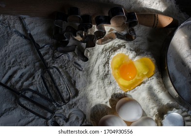 Flour On A Table With A Cookie Cutter In The Shape Of A Man And A Whisk For Kneading, Eggs. Pit In Flour In The Form Of A Heart Into Which An Egg Is Broken