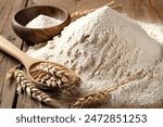 The  flour pile and wheat grains in wooden spoon and bowl on wooden background