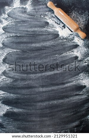 Flour is poured on a black background and there is a rolling pin made of wood. Baking background with free space for your text. Cooking from flour, background. Copy space.