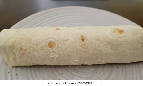 Flour Tortilla Wrapped Burrito On Glass White Plate