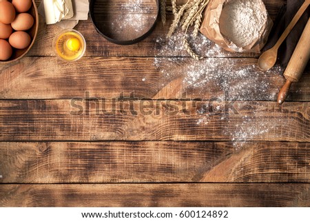 Flour with wheat, eggs, rolling pin, spoon and butter on wooden background, top view with copy space. Ingredients for bakery products