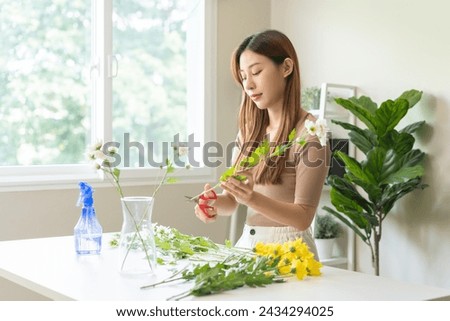 Flower arrangement, happy beautiful asian young woman florist hand making flower in vase, creating bouquet on the table, arranging indoors decor in living room, handmade house interior or decoration.