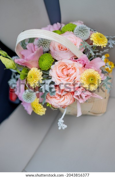 Flower arrangement in\
Wicker basket. Beautiful bouquet of mixed flowers on a car\'s seat,\
with modern, beige color interior.\
Concept: Small flower shop,\
Flowers delivery. 