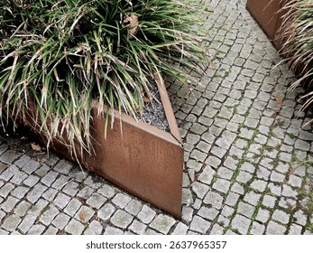 the flower bed is bordered by a rusty sheet metal design. perennials and grass bloom in the flowerbed. paving stone cubes between two flowerbeds. are benches