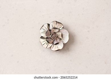 A flower brooch made of natural gray mother-of-pearl lies on a light modern gray white concrete background. Jewelry for women on a light background.