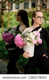 Flower composition with hydrangea, peonies, carnations, gypsophila in hat box in woman's hands. Young girl posing with flowers in hat box near mirror doors.