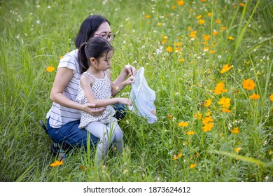 In a flower field, Mother and cute little Asian girl finding  insects in the net.