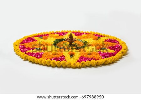 Flower rangoli for Diwali or Pongal made using marigold or zendu flowers and red rose petals over white background with Clay Oil Lamp in the middle, selective focus