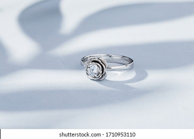 Flower shaped silver wedding ring with big diamond on blue background with leaves shadows. Original design white gold ring