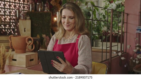 Flower Shop Business Owner Inside Shop Wearing Apron. A Middle Aged Female Entrepreneur Owner Of Local Business